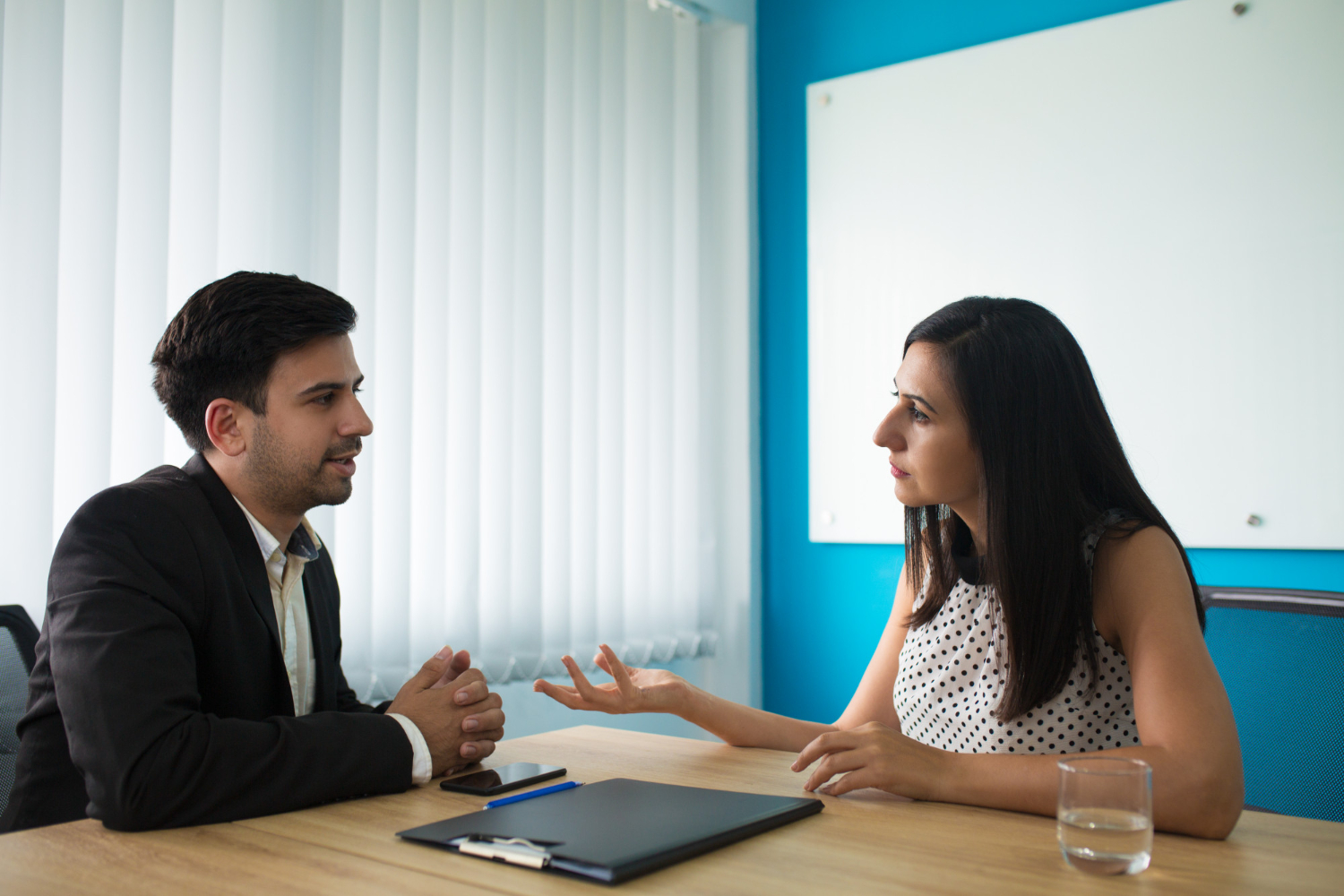 A man and woman sitting at a table in an office setting, working on a laptop and collaborating.