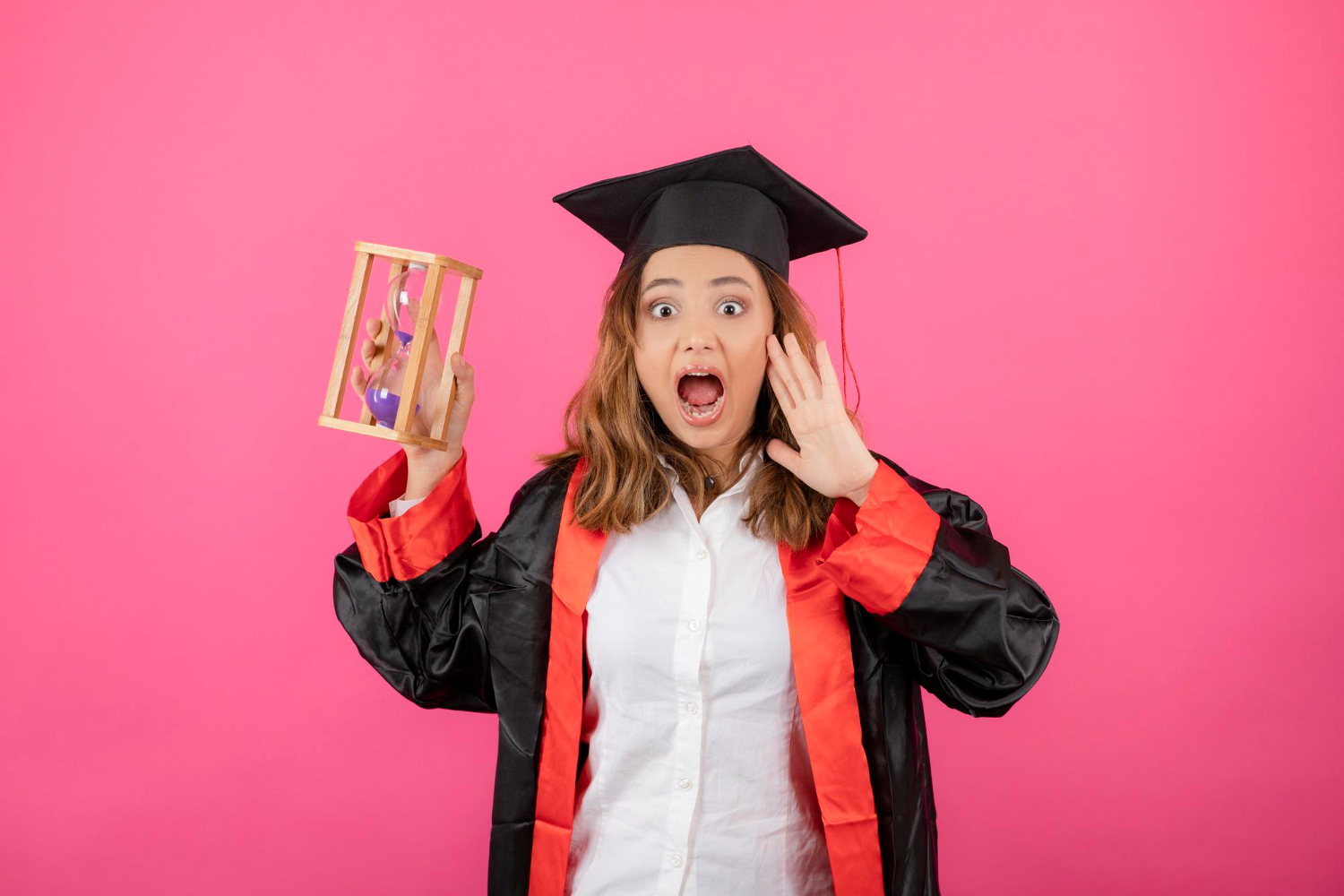 A woman in a graduation gown and mortarboard is smiling while holding a wooden cage indoors.