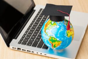 A globe wearing a graduation cap sits on a laptop keyboard, symbolizing global education and online learning.