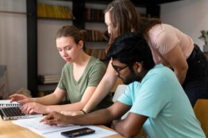 A group of three people collaborates around a laptop, focusing intently on their work in a cozy indoor setting.