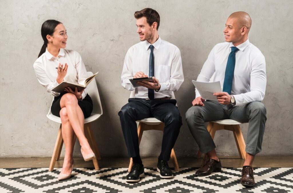 Three professionals sit in a modern setting, engaged in discussion while taking notes, dressed in business attire.