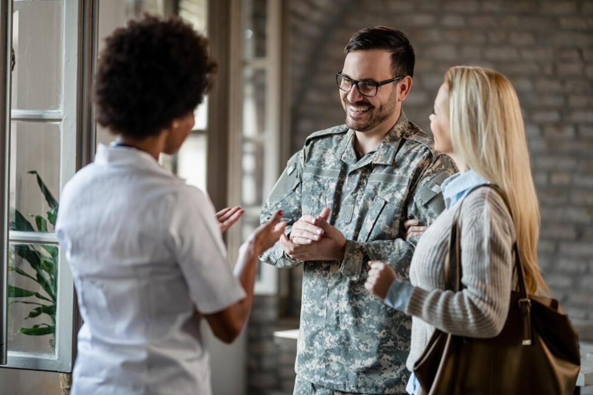 A military personnel in uniform engages in conversation with two women in a well-lit, spacious room with brick walls.