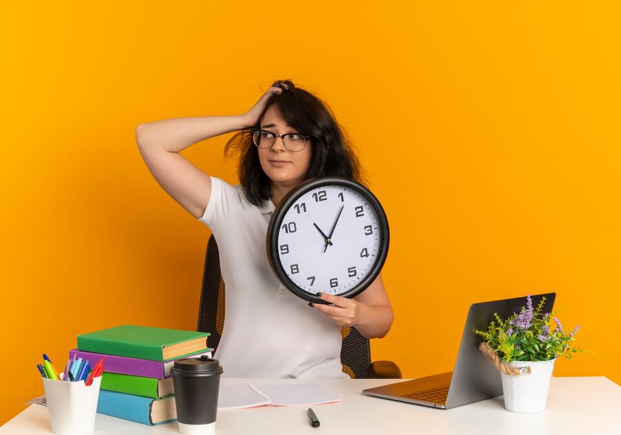 A person holding a clock, surrounded by colorful books, a laptop, a coffee cup, and a small plant, against a bright orange background.