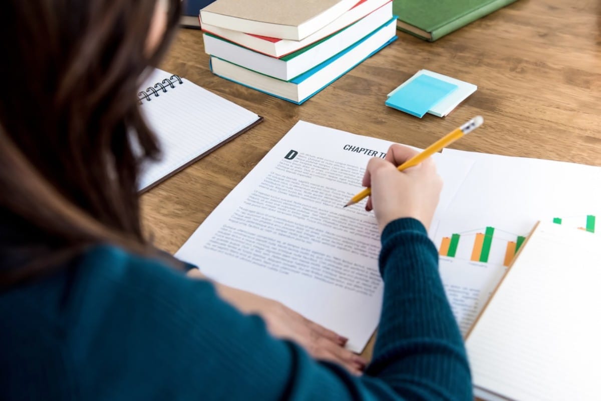 A person writes notes with a pencil on a document titled