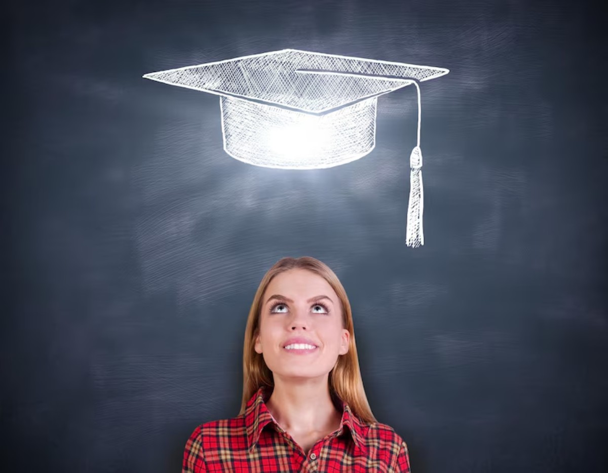 A person in a red plaid shirt stands in front of a chalkboard, with a glowing illustration of a graduation cap above their head.