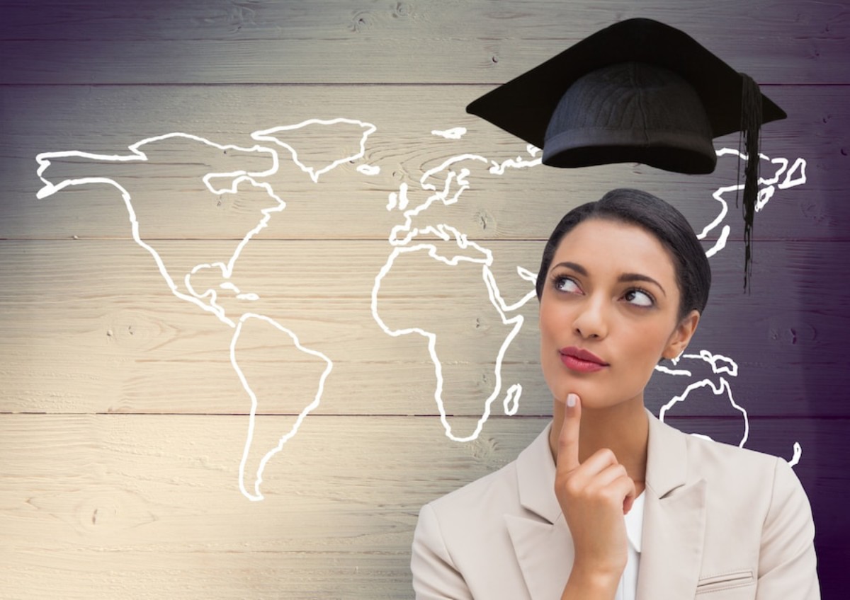 A graduation cap is positioned above a thoughtful individual against a wooden background featuring a white world map outline.
