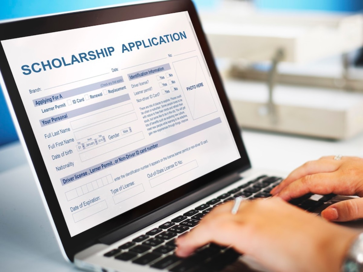 A person fills out a scholarship application on a laptop, with sections for personal details and identification information visible.