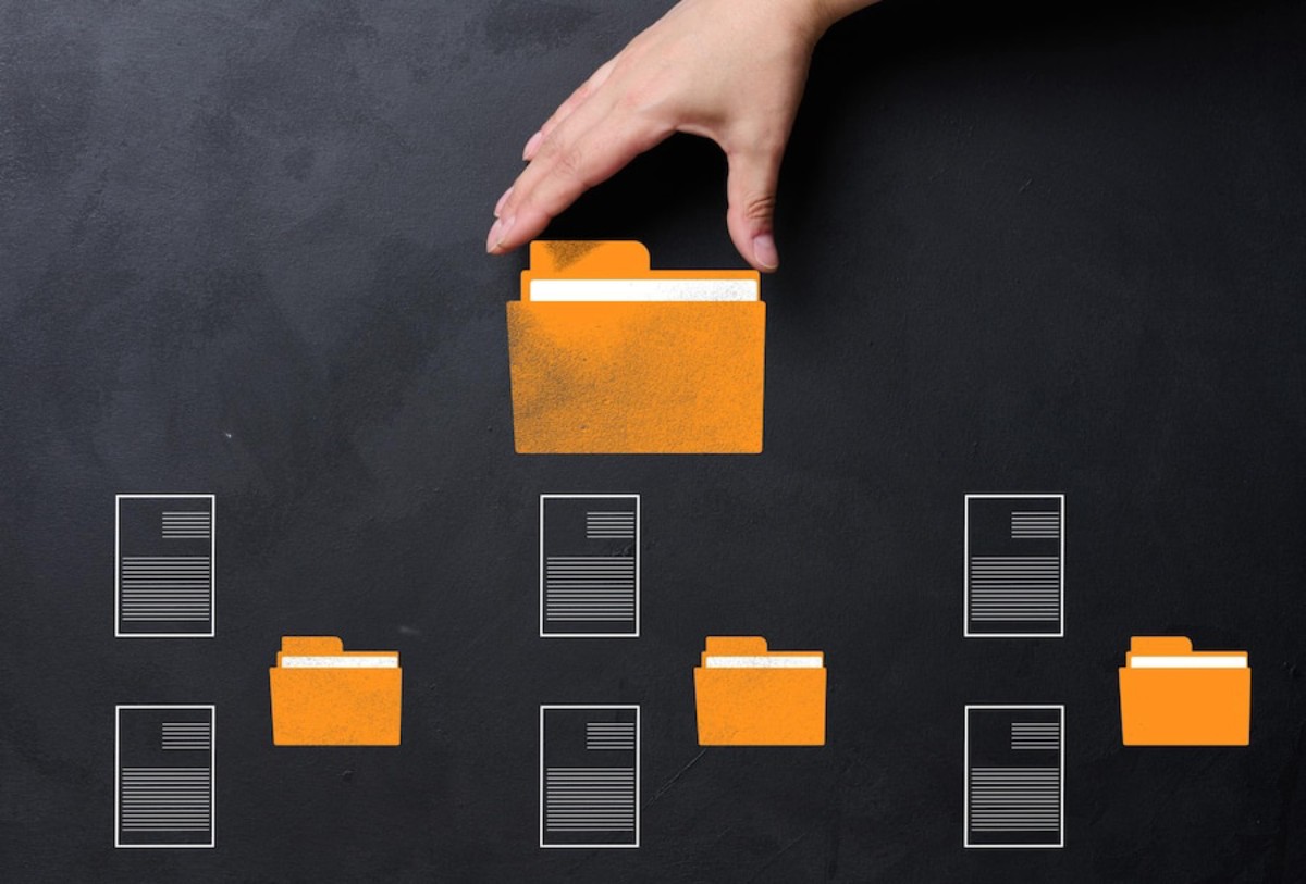 A hand places an orange folder above several document icons on a dark background, symbolizing organization and file management.