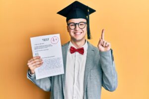 A proud graduate in a cap and bow tie holds up a test paper marked with an A+, smiling against a bright yellow background.