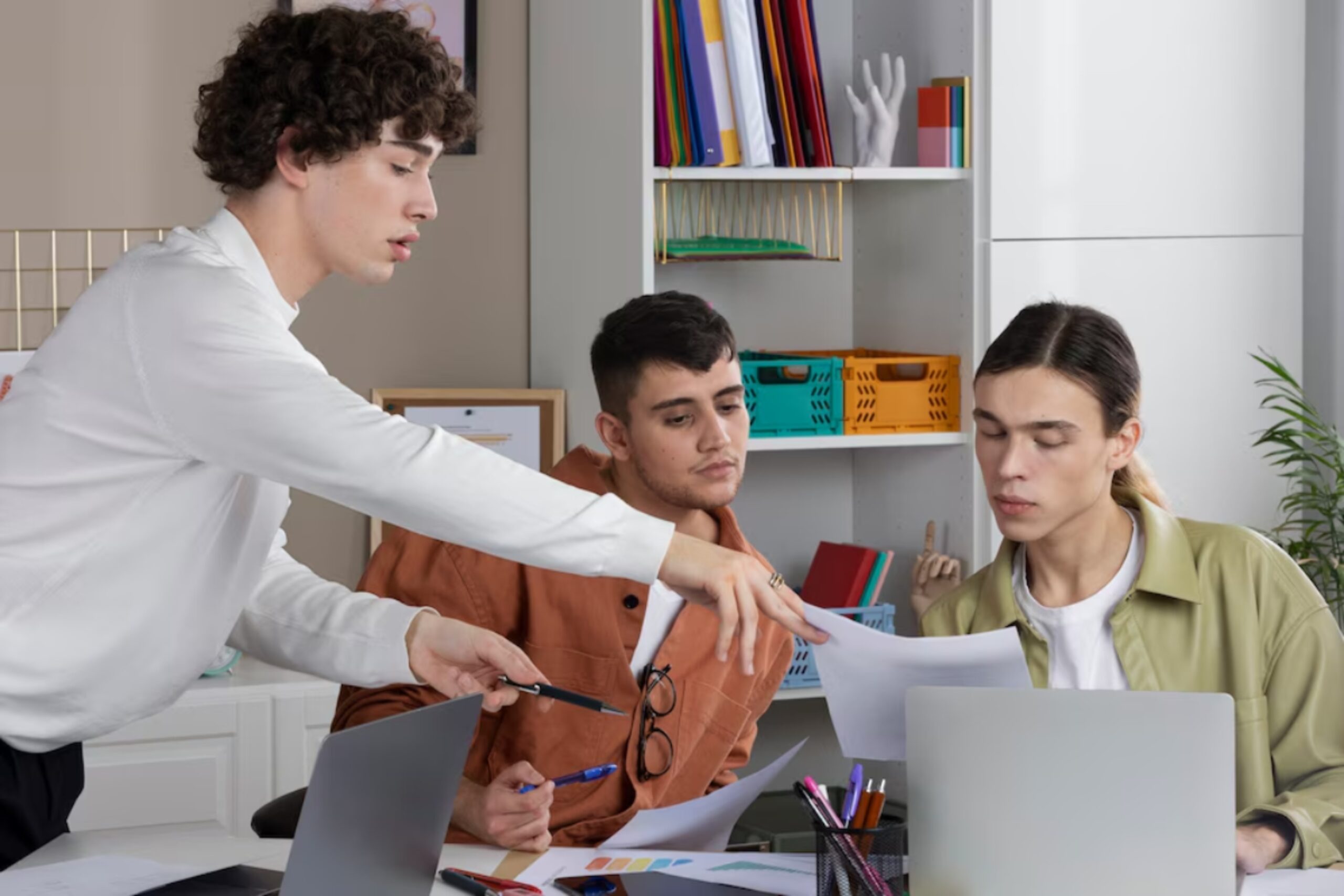 A diverse team collaborates around a desk with laptops and paperwork, engaged in a discussion within a modern office space.